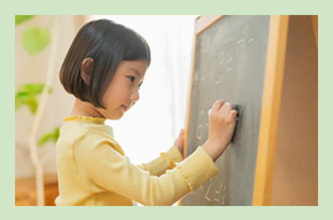 黒板に文字を書く黄色い服の子どもの写真